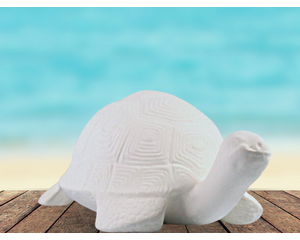 Handmade ready to paint ceramic turtle on a table by the ocean.  It is facing slightly toward the right.  The detail on the shell is visible